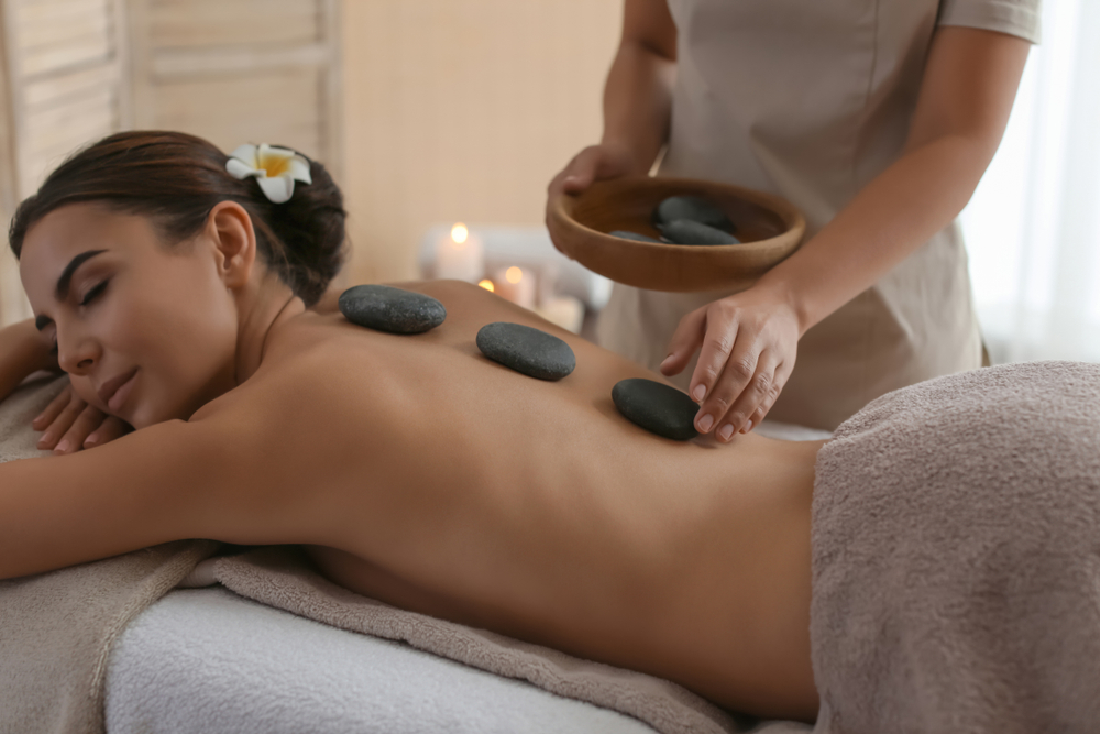 Close-up of a massage therapist's hands using warm stones to gently massage a client's shoulders, showcasing the relaxing and therapeutic environment of the massage center.